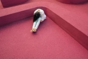 Person lying alone on a red surface, symbolising stress, emotional overload, and exhaustion.